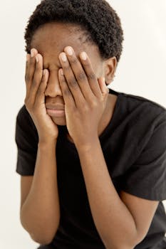Portrait of a young woman covering her face with hands, expressing distress indoors.